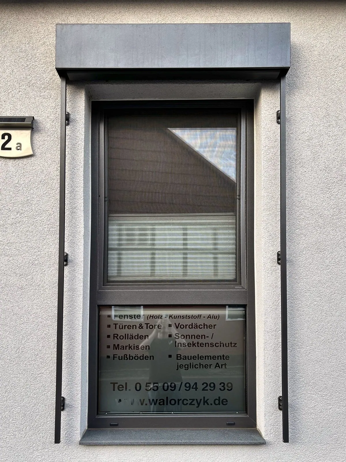 Hohes Fenster in Anthrazit mit Raffstore-Kasten und seitlichen Führungsschienen, Scheibe mit MW-Beschriftung