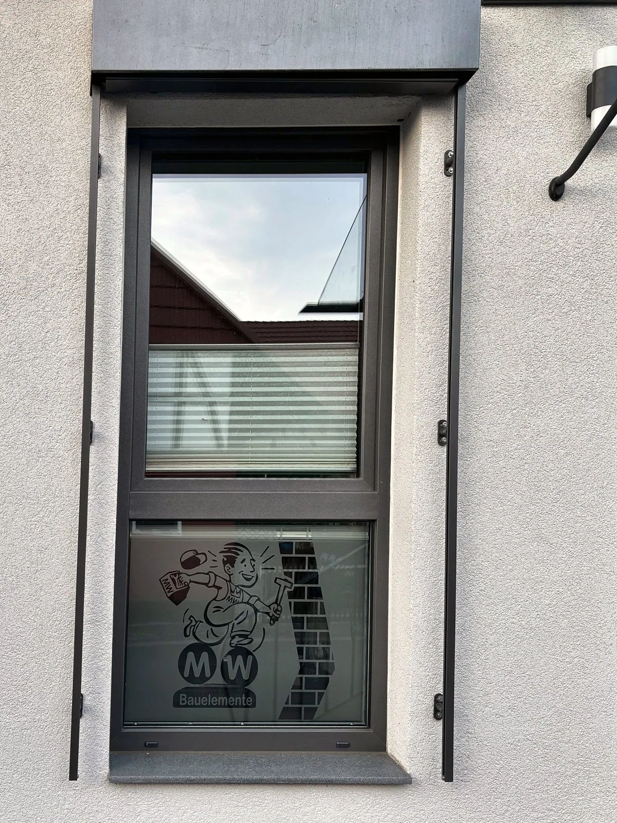 Fenster in Anthrazit mit Raffstore-Kasten, auf der Scheibe das MW-Maskottchen