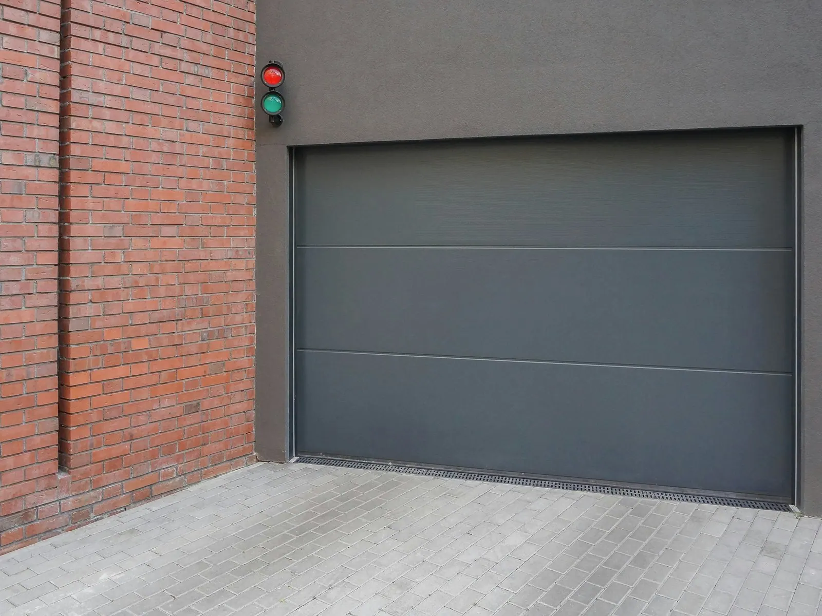 Glattes Sektional-Garagentor in Anthrazit neben einer roten Klinkerwand